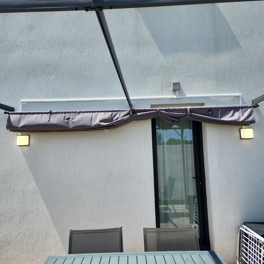 Terrasse avec store banne gris anthracite et porte-fenêtre noire, murs blancs et éclairages muraux